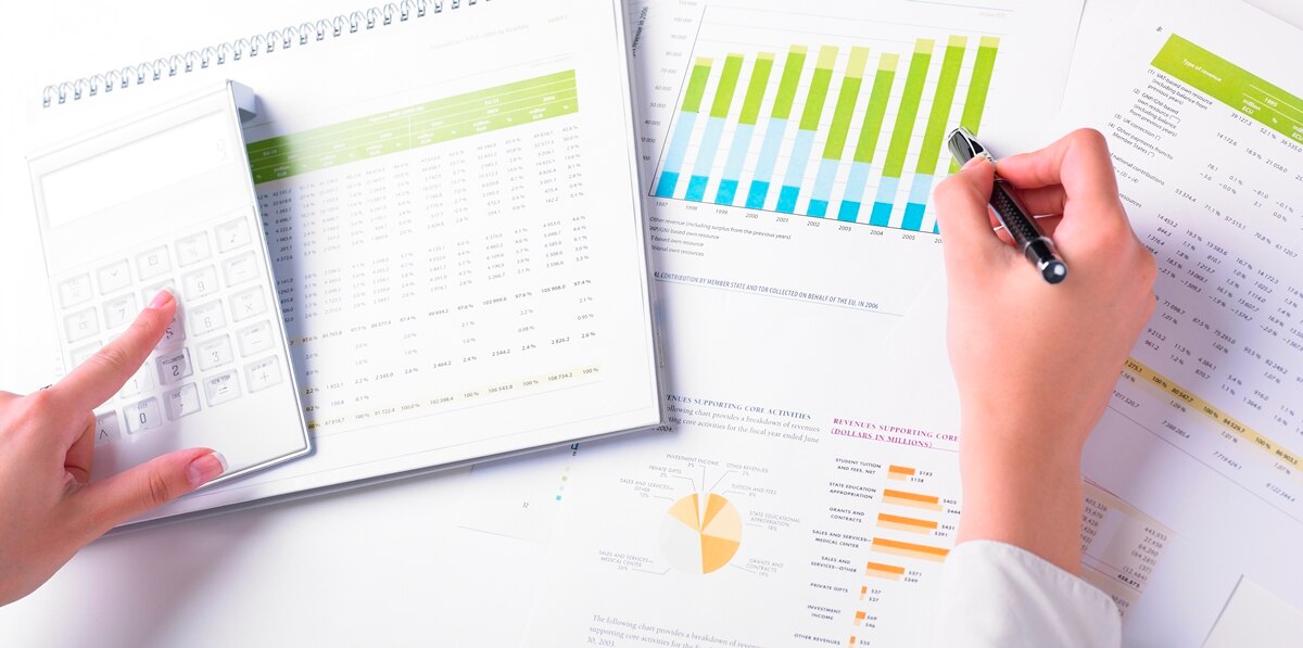 Finger using calculator while other hand holds a pen pointing to a graph