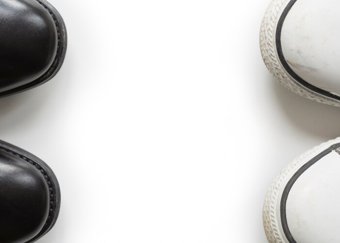 Pair of black dress shoes facing a pair of grey converse