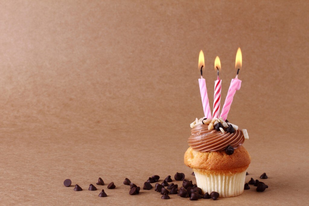 Cupcake with three lit candles surrounded by chocolate chips
