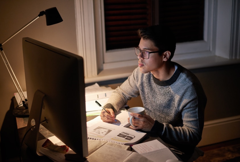 Student revising a paper late at night in the glow of a computer screen