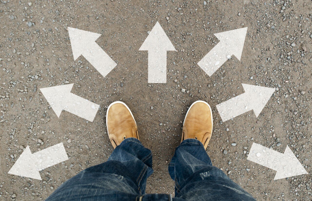 Feet with tan shoes on pavement with arrows pointing in multiple directions
