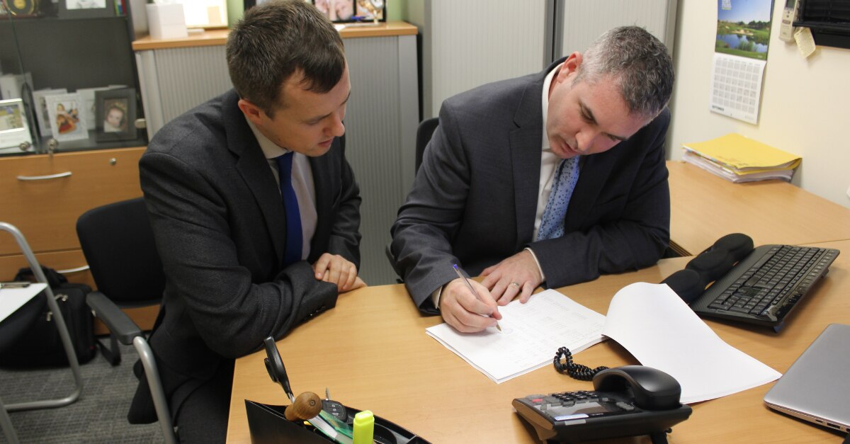 John and another male employee writing on and looking at a paper on a desk