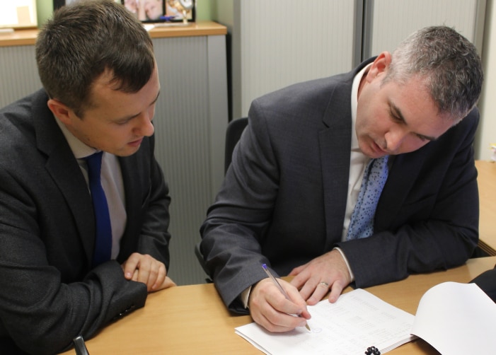 John and another male employee writing on and looking at a paper on a desk