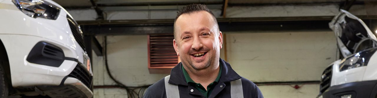 Enterprise Mobility Mechanic in the UK dressed in high visibility overalls and standing in a workshop. 