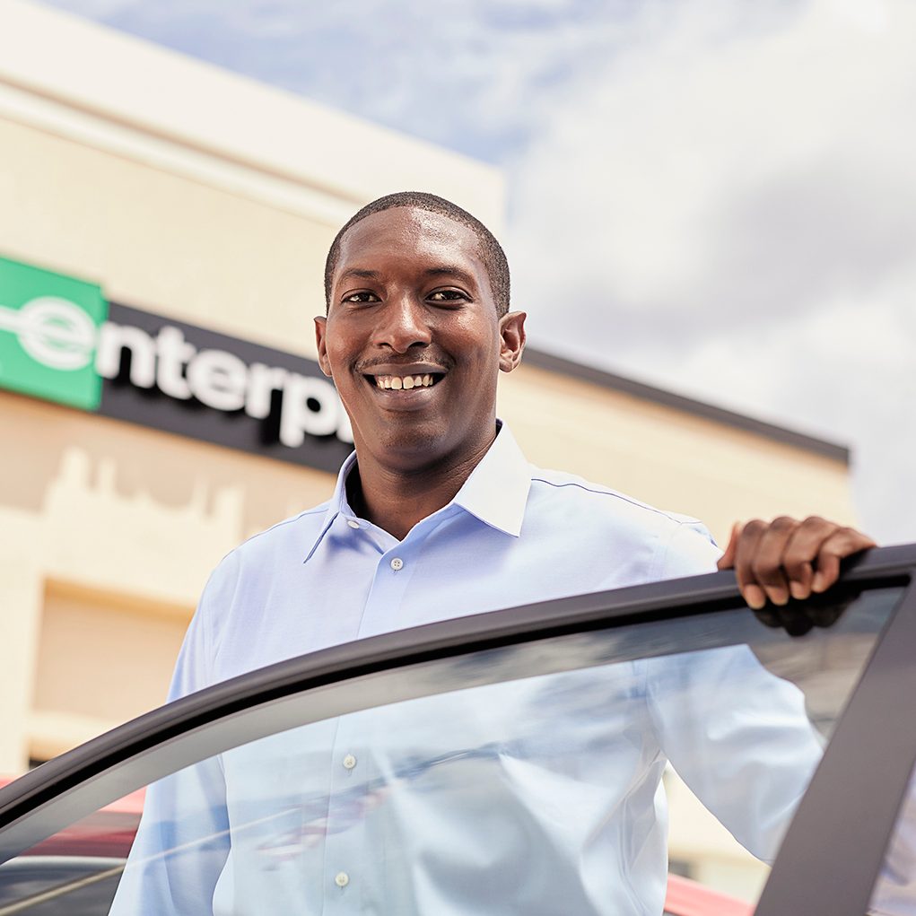 Team member smiling while leaning over an open car door 