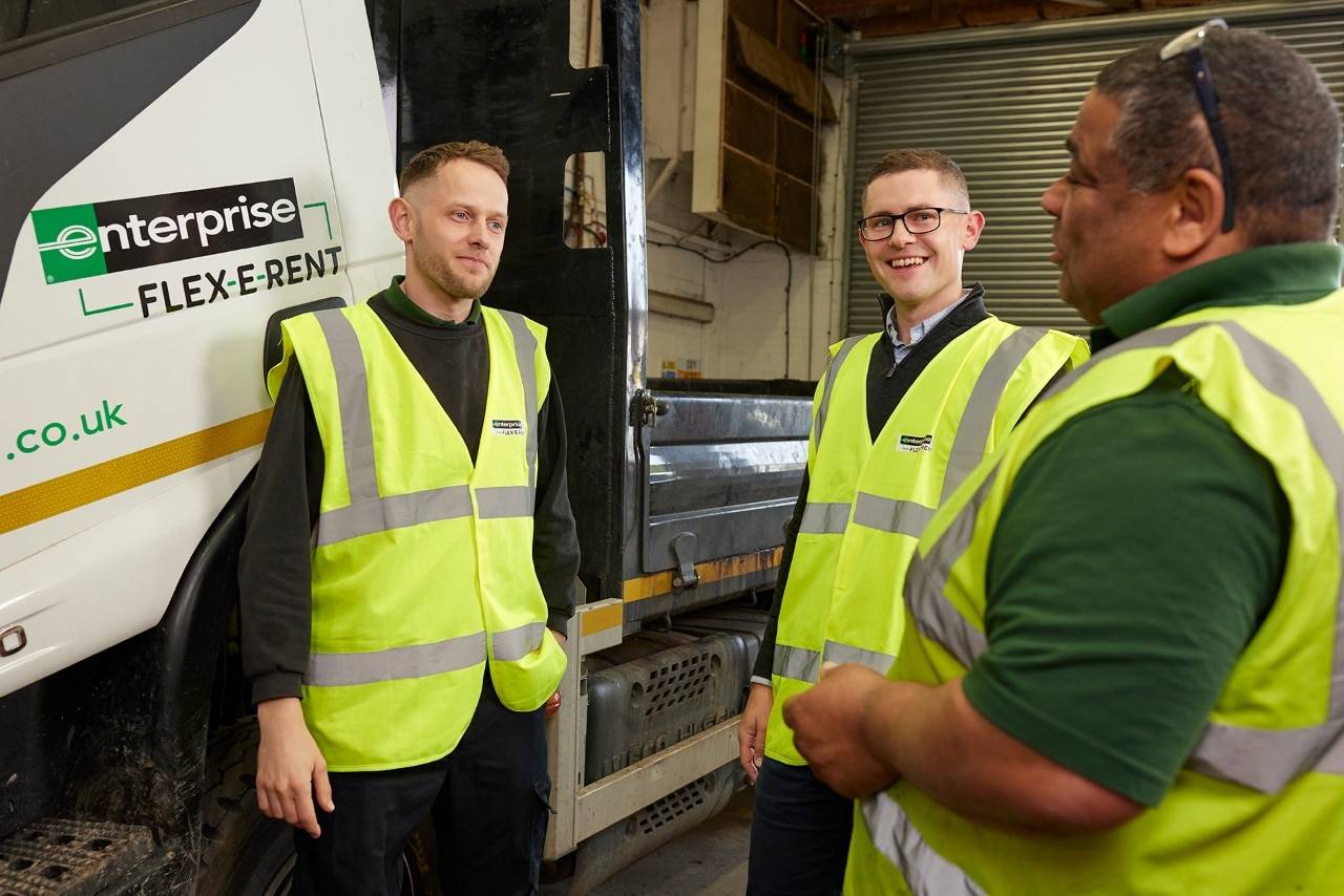 Three Enterprise Mobility team members wearing high-visibility jackets talking in the workshop.