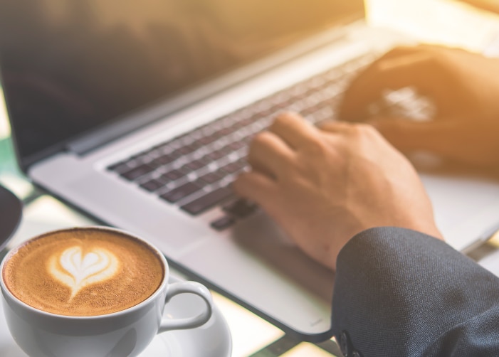Hands typing on a Macbook with coffee and cake on table
