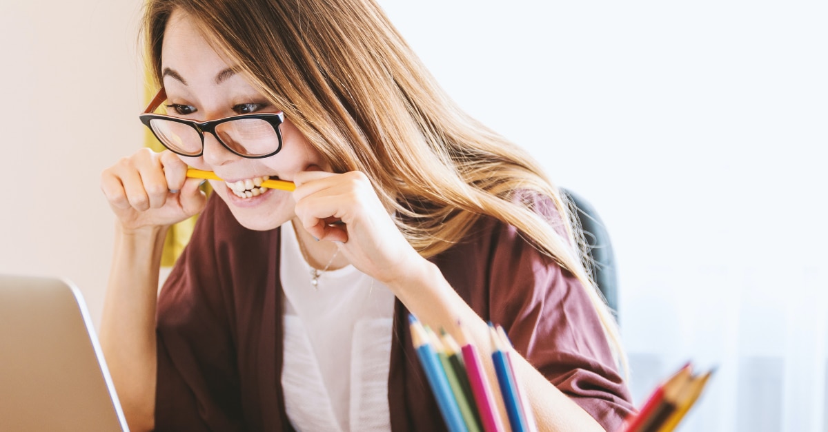 Stressed girl biting pencil while looking at laptop