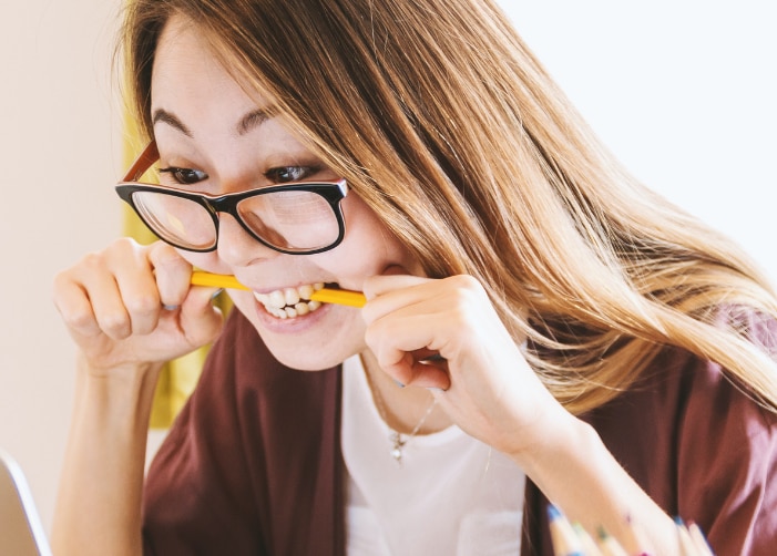 Stressed girl biting pencil while looking at laptop