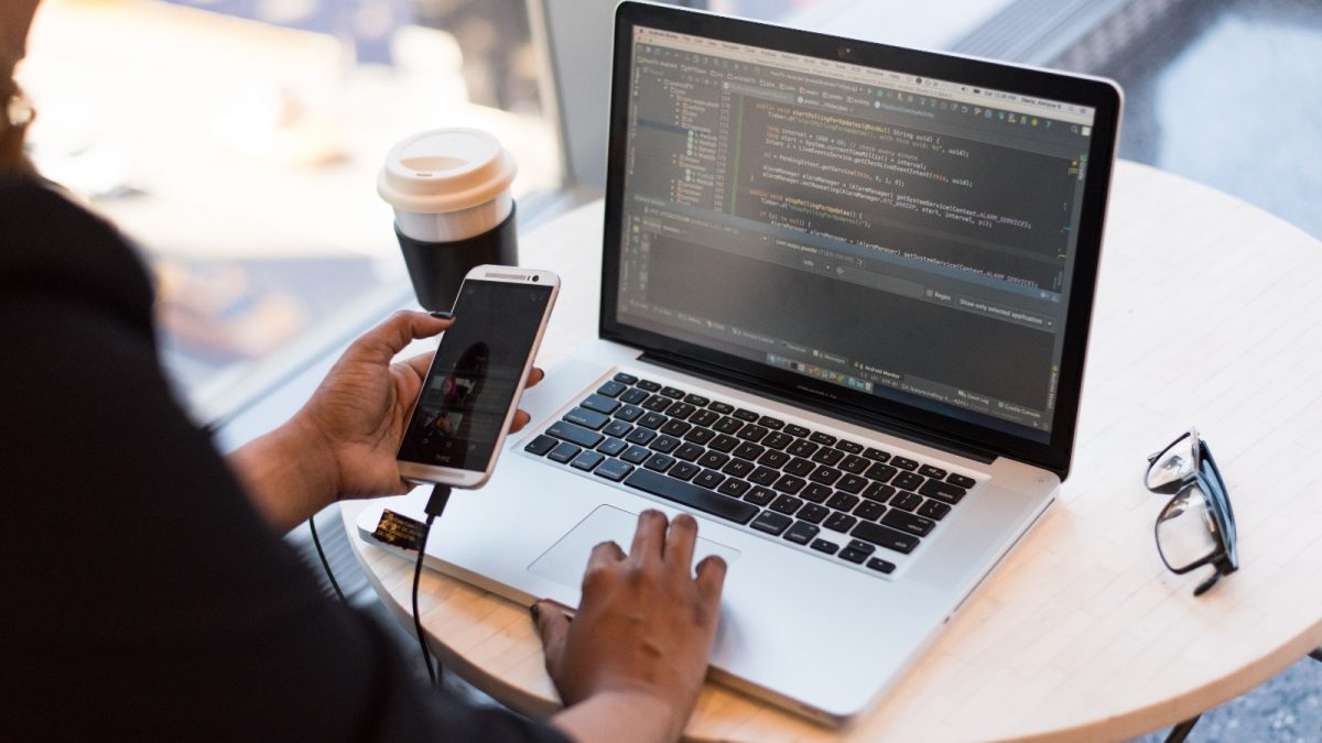 Person looking at Macbook while using their cellphone