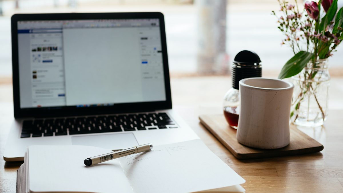 Open laptop and notebook with pen and coffee mug on desk