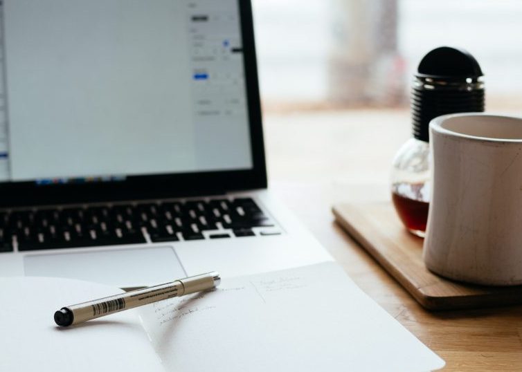 Open laptop and notebook with pen and coffee mug on desk