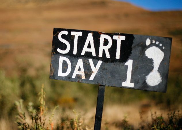 Sign in the wilderness that is painted with a human footprint and says "Start day 1"