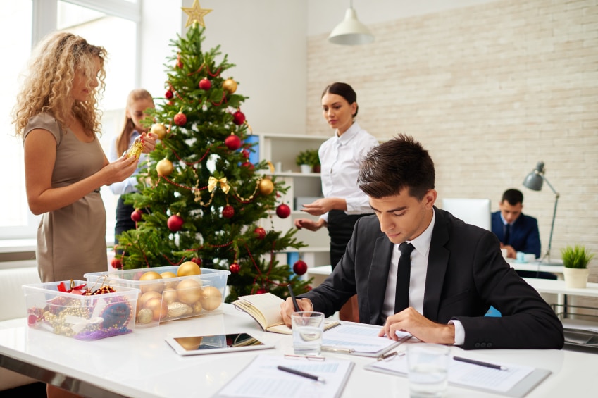 Businessman finishing work with document, his female colleagues decorating Christmas tree