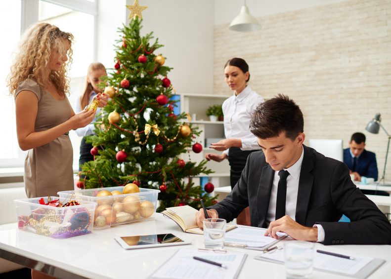 Businessman finishing work with document, his female colleagues decorating Christmas tree