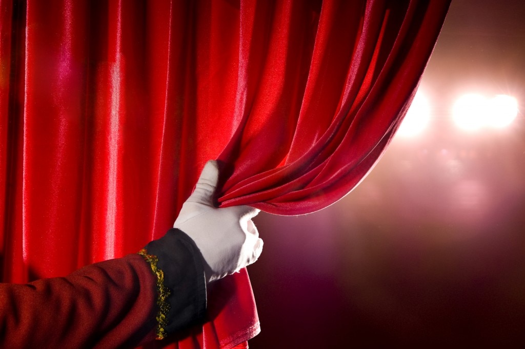 Hand with white glove opening red curtain