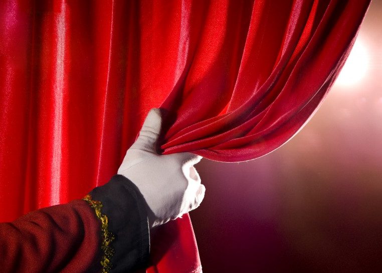Hand with white glove opening red curtain