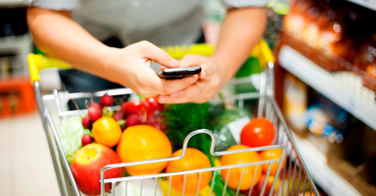Texting while pushing shopping cart full of fruits and vegetables