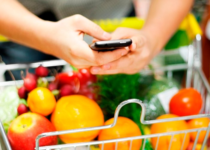 Texting while pushing shopping cart full of fruits and vegetables