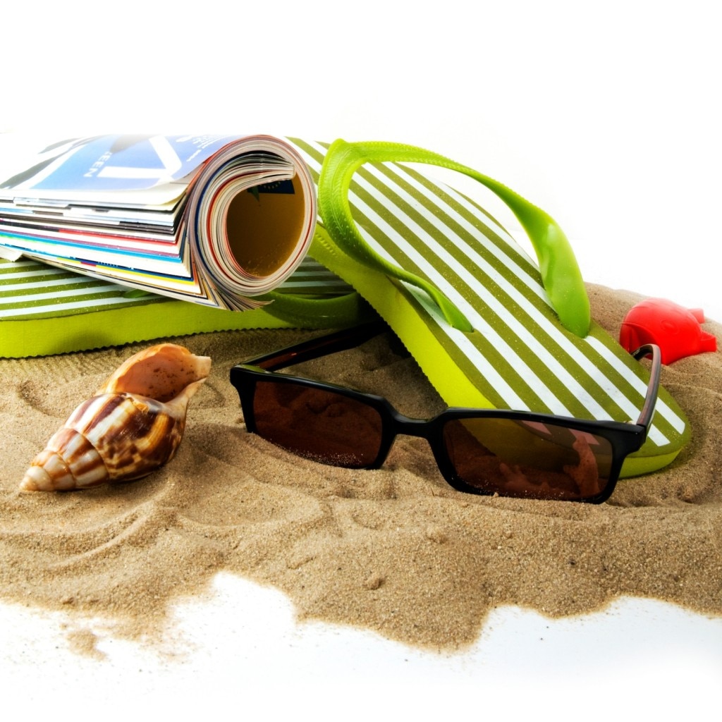 Sunglasses, a magazine, sandals, and a seashell on the beach