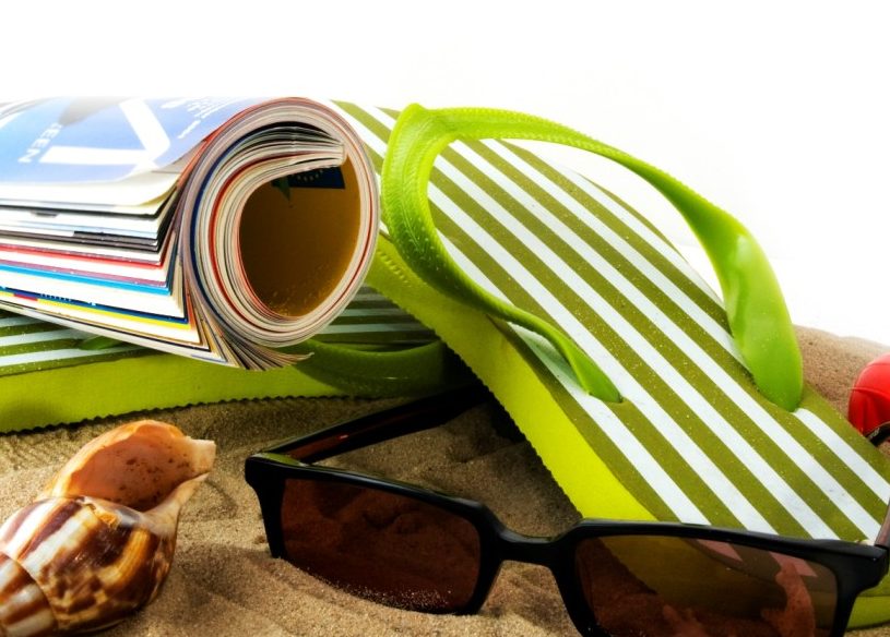 Sunglasses, a magazine, sandals, and a seashell on the beach