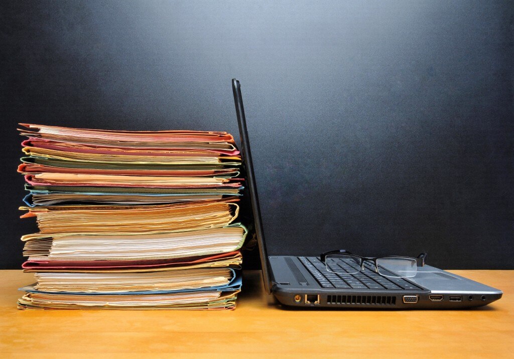 Laptop with glasses on keyboard next to stack of folders