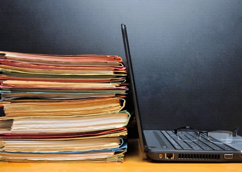 Laptop with glasses on keyboard next to stack of folders