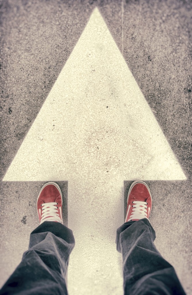 Feet standing across arrow painted on road