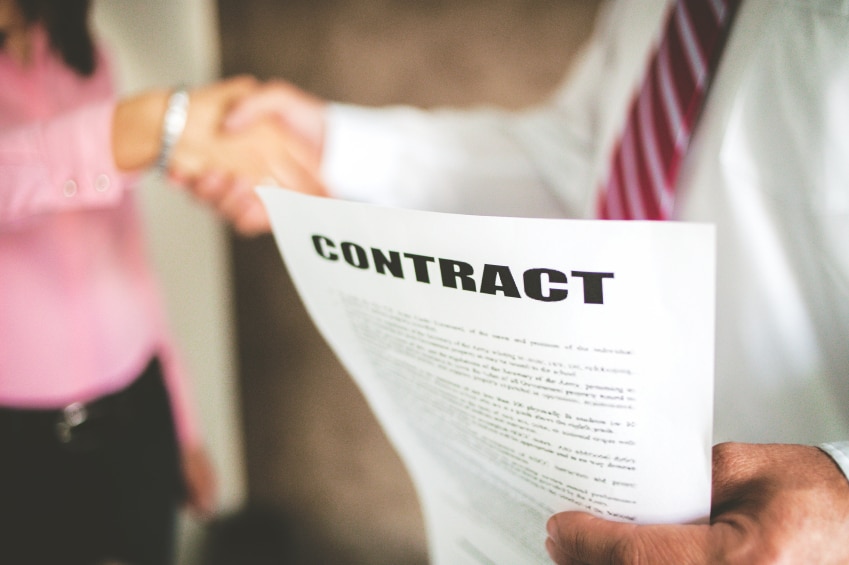 Blurred people shaking hands with a paper that says "Contract" in focus