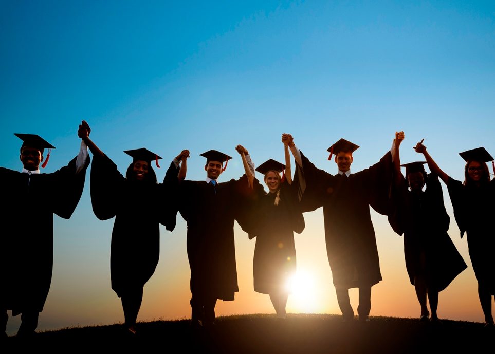 Students in graduation caps and gowns walking into the sunset