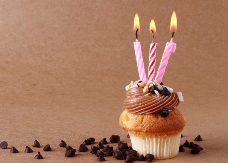 Cupcake with three lit candles surrounded by chocolate chips