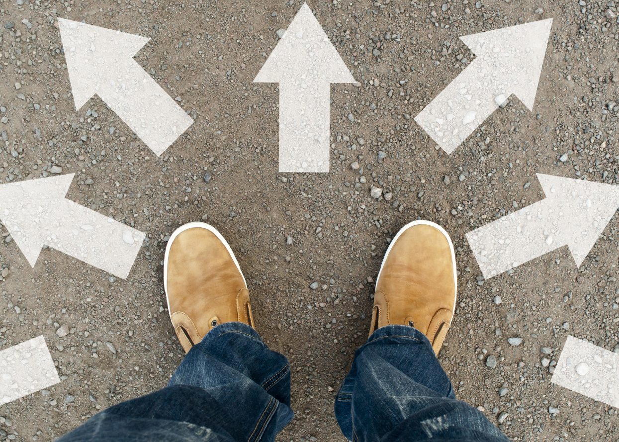 Feet with tan shoes on pavement with arrows pointing in multiple directions