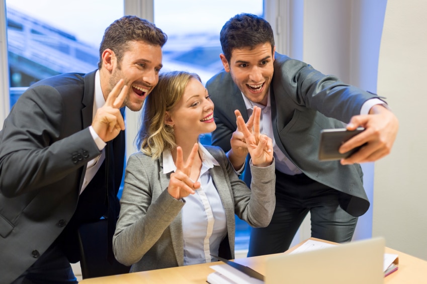 3 people making peace signs while taking a selfie in professional clothing