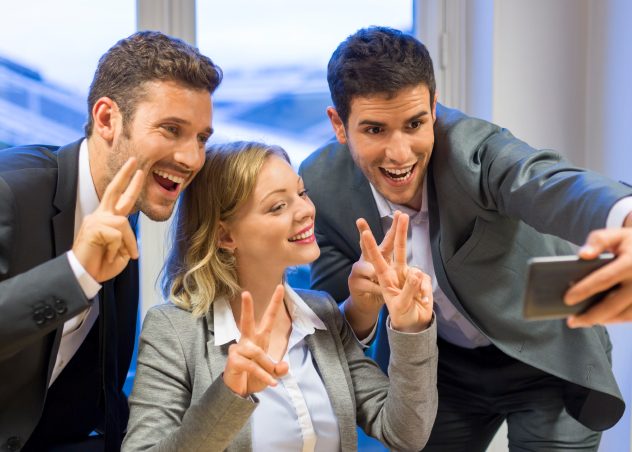 3 people making peace signs while taking a selfie in professional clothing