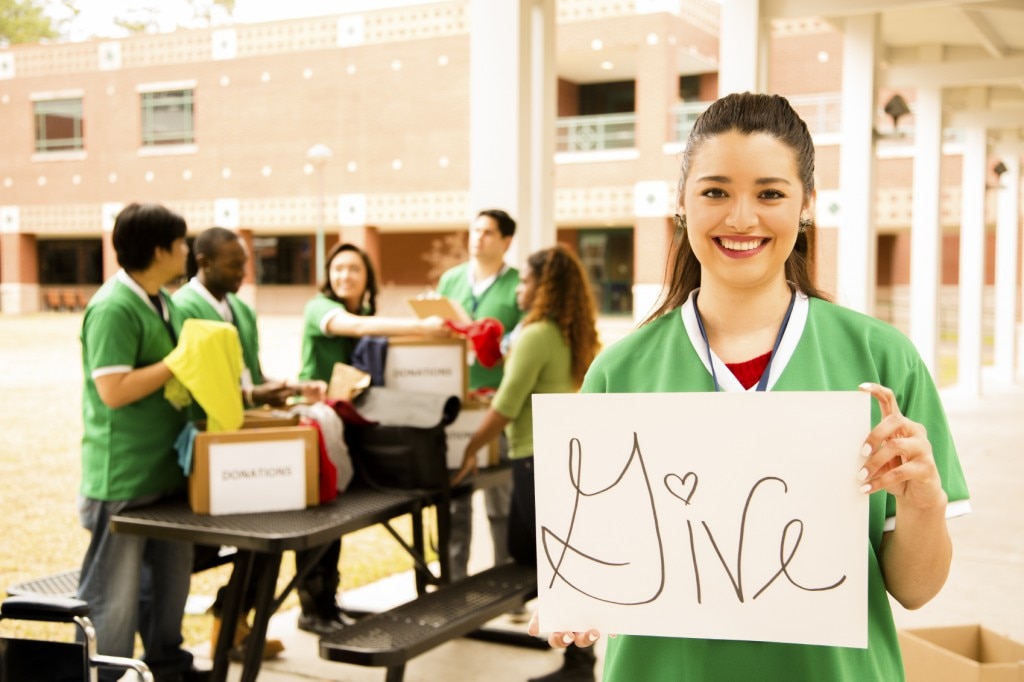 Girl holding sign that says "Give" while friends pack boxes of donations