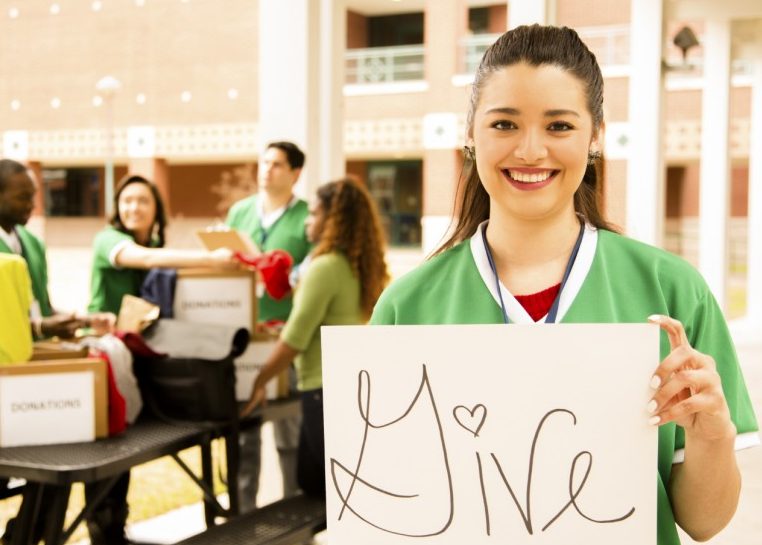 Girl holding sign that says "Give" while friends pack boxes of donations