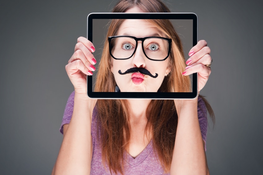 Girl holding iPad in front of her face with a picture of her face with a fake mustache and glasses