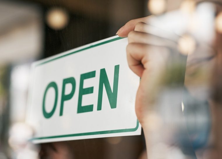 Hands flipping green and white "OPEN" sign