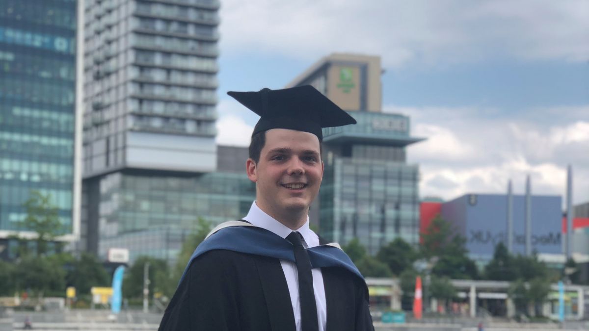 Tommy in graduation cap and gown in front of skyscrapers