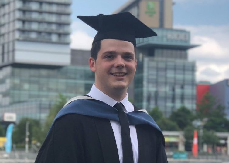 Tommy in graduation cap and gown in front of skyscrapers