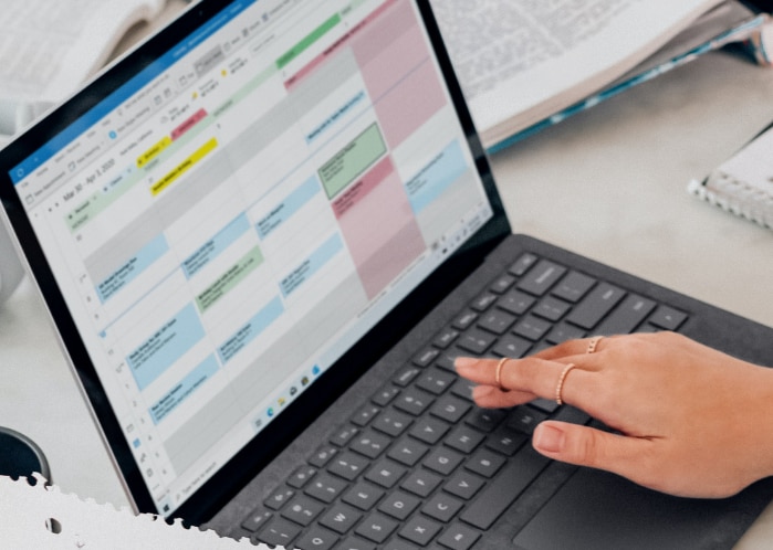 Hand typing on laptop with Outlook calendar open
