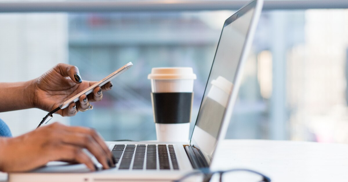 Holding a phone and typing on a MacBook in a coffee shop