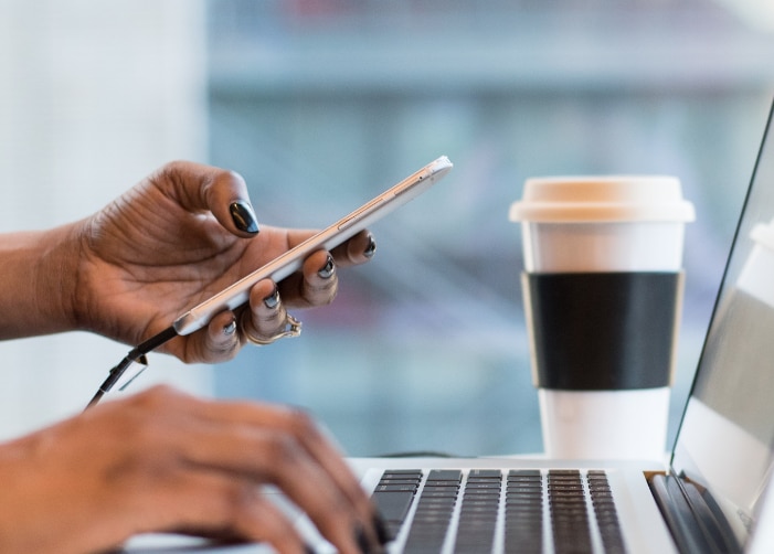 Holding a phone and typing on a MacBook in a coffee shop